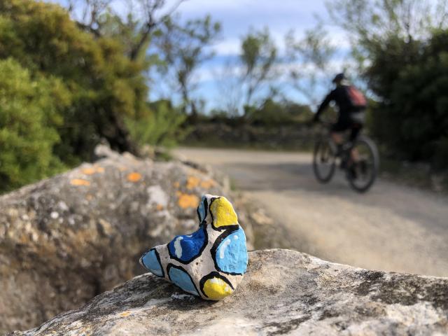 Photo d'un cailloux peint et en 2ème plan un cycliste qui passe