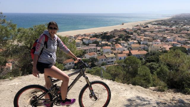 Foto van een jong meisje op haar fiets met het strand op de achtergrond en Leucate Plage gezien vanaf de top van de klif.